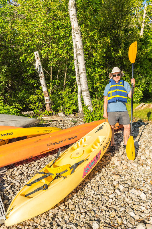 Man in life vest holding kayak handle and paddle while standing on shoreline
