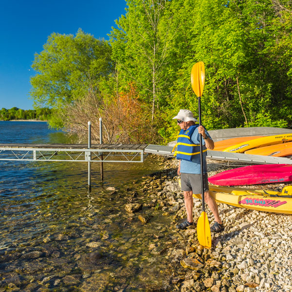 Kayaker holding paddle at the shoreline with many kayaks