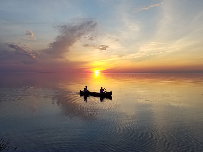 Two people canoeing across lake as sun sets