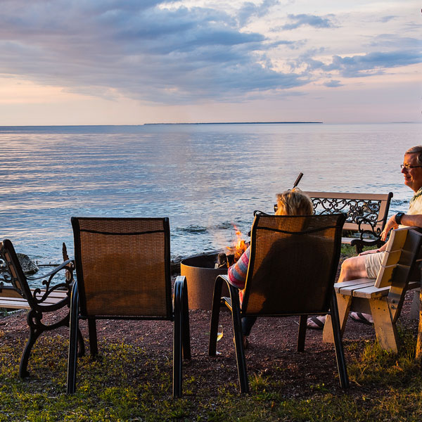 Door county Resort guest relaxing around a fire on chairs and benches by the water at sunset