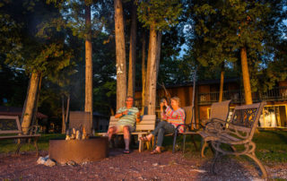 Two people sitting on benches by a fire pit in front of Beachhouse