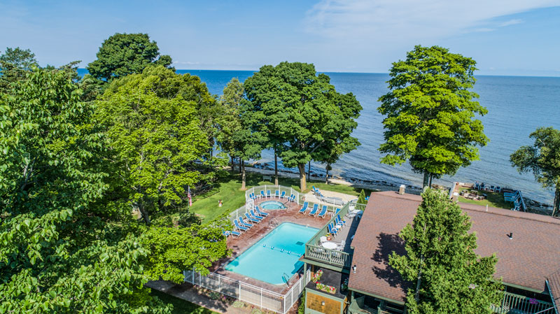 Aerial view of outdoor pool surrounded by trees with bay in the background