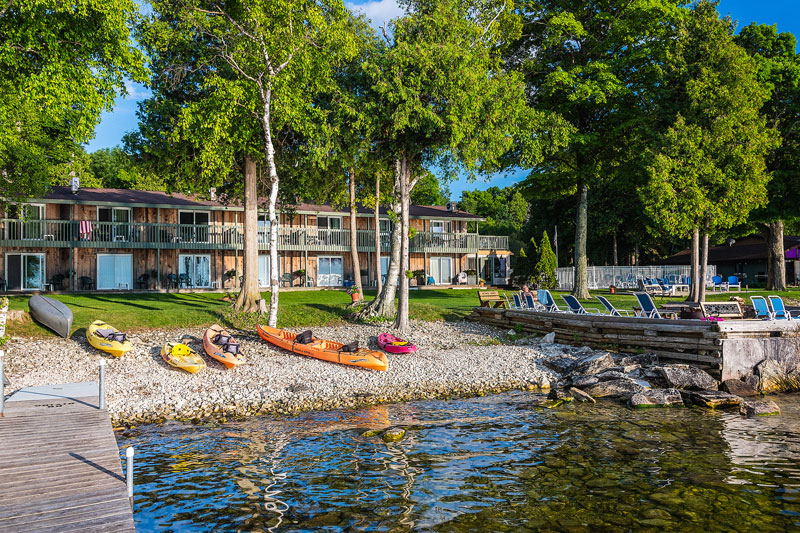 Several kayaks along the waters edge with the shoreside motel in the Background