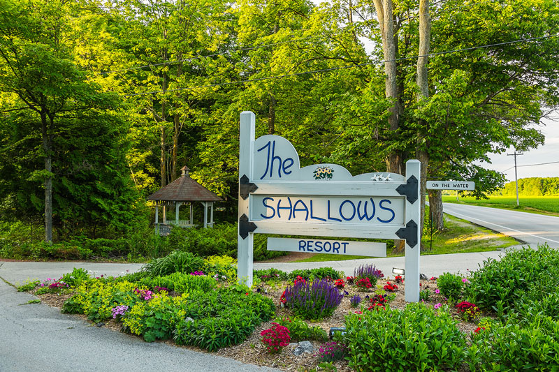 Shallows Resort sign at entrance surrounded by flowers and small bushes