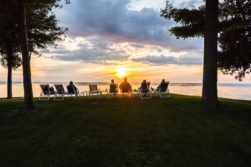 Group of people sitting on deck chairs watching the sun set over the bay